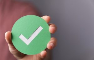 A man holding a green check mark on a grey background.
